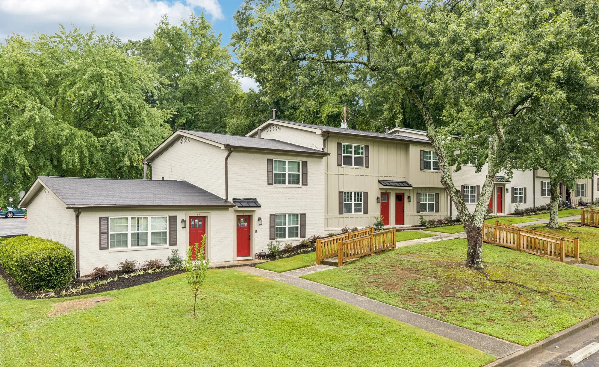 Townhomes with red doors among mature trees.